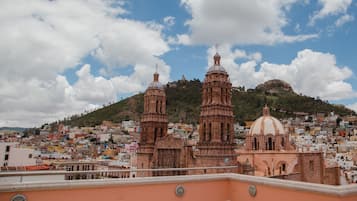 A cityscape with a prominent church featuring two towers and a dome, set against a backdrop of a hill and a clear sky.