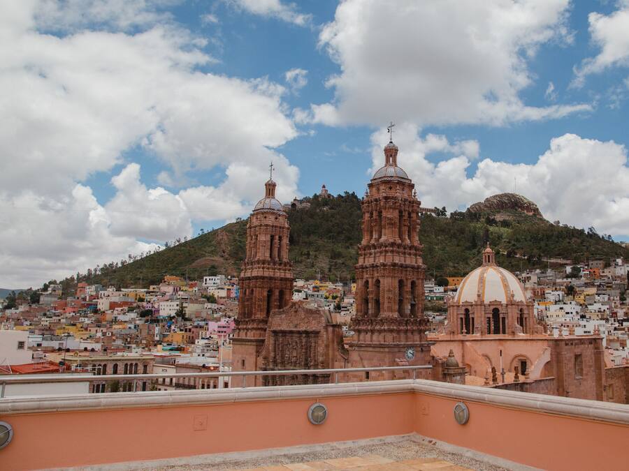 A cityscape with a prominent church featuring two towers and a dome, set against a backdrop of a hill and a clear sky.