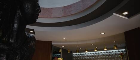 Un interior moderno con techo curvo, iluminación empotrada y una zona de recepción con un muro decorativo y un jarrón de flores.