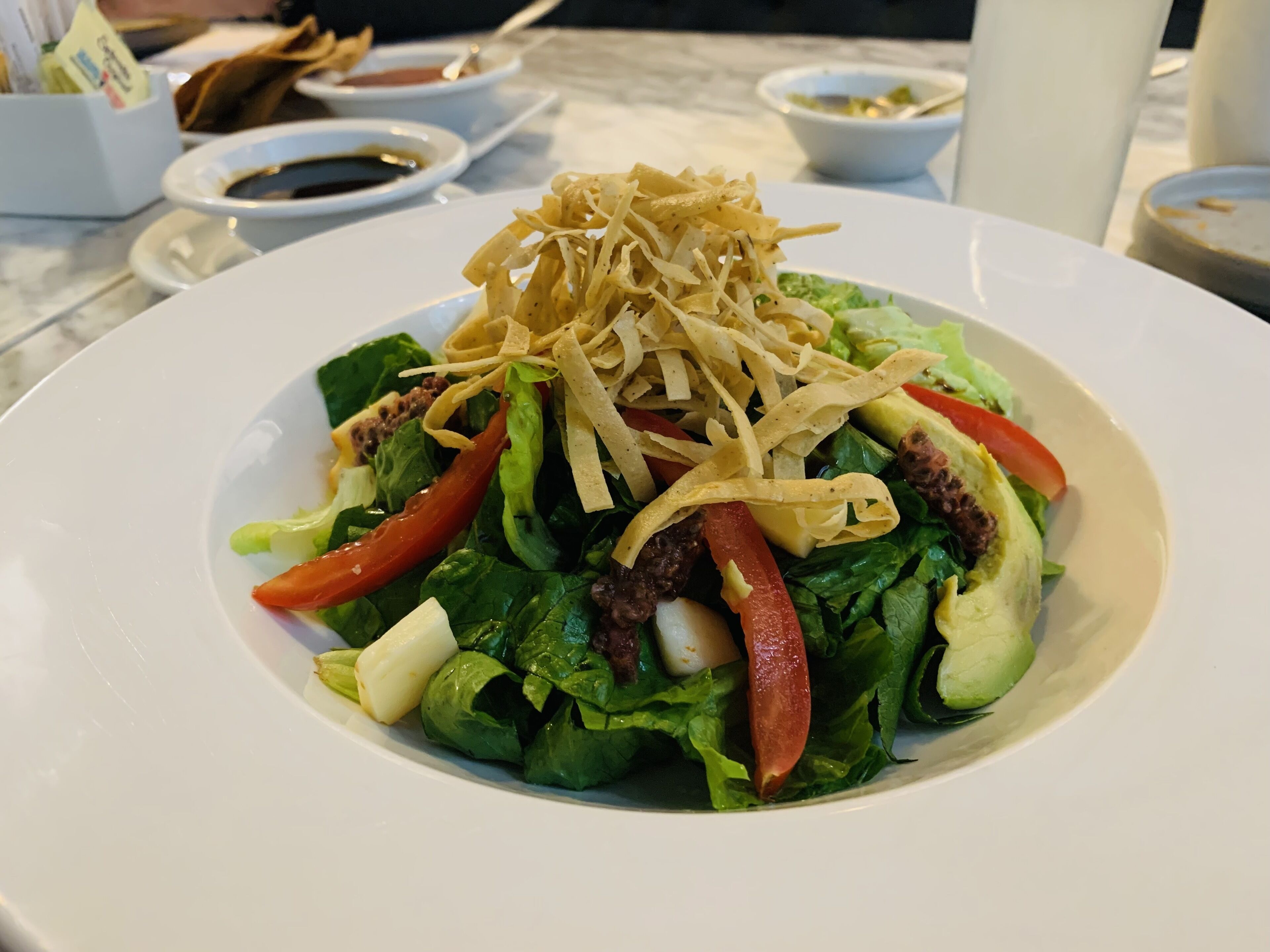Ensalada con varias verduras y queso rallado sobre un plato blanco.