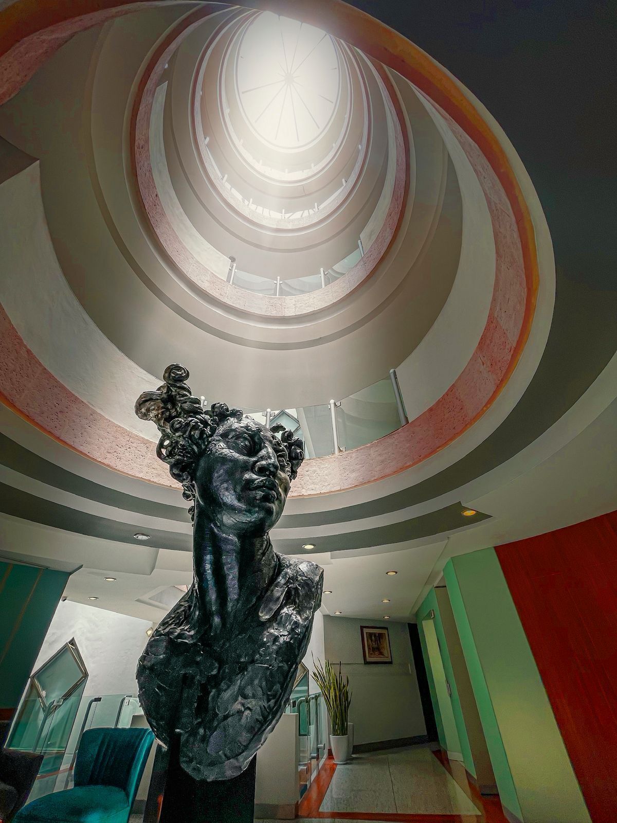 A sculpture in a lobby with a circular ceiling design and a skylight.