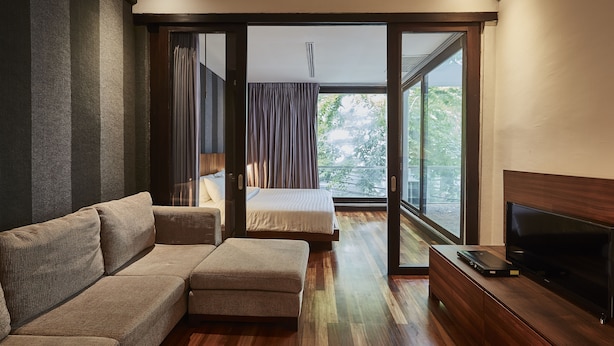 A modern bedroom with a sofa, a bed, a TV on a wooden cabinet, and a sliding glass door leading to a balcony. - Luxx at Silom (Bangkok)
