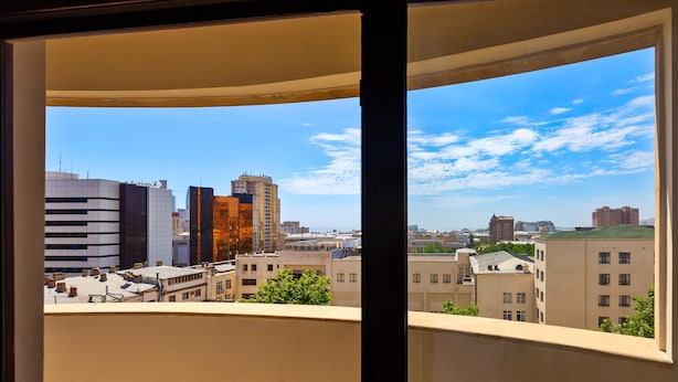A cityscape through a window with modern buildings, a clear sky, and a view of the urban landscape.