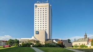 A tall hotel with a modern design, a clear sky, and a church in the background. - Clarion Congress Hotel Ceske Budejovice (Ceske Budejovice)