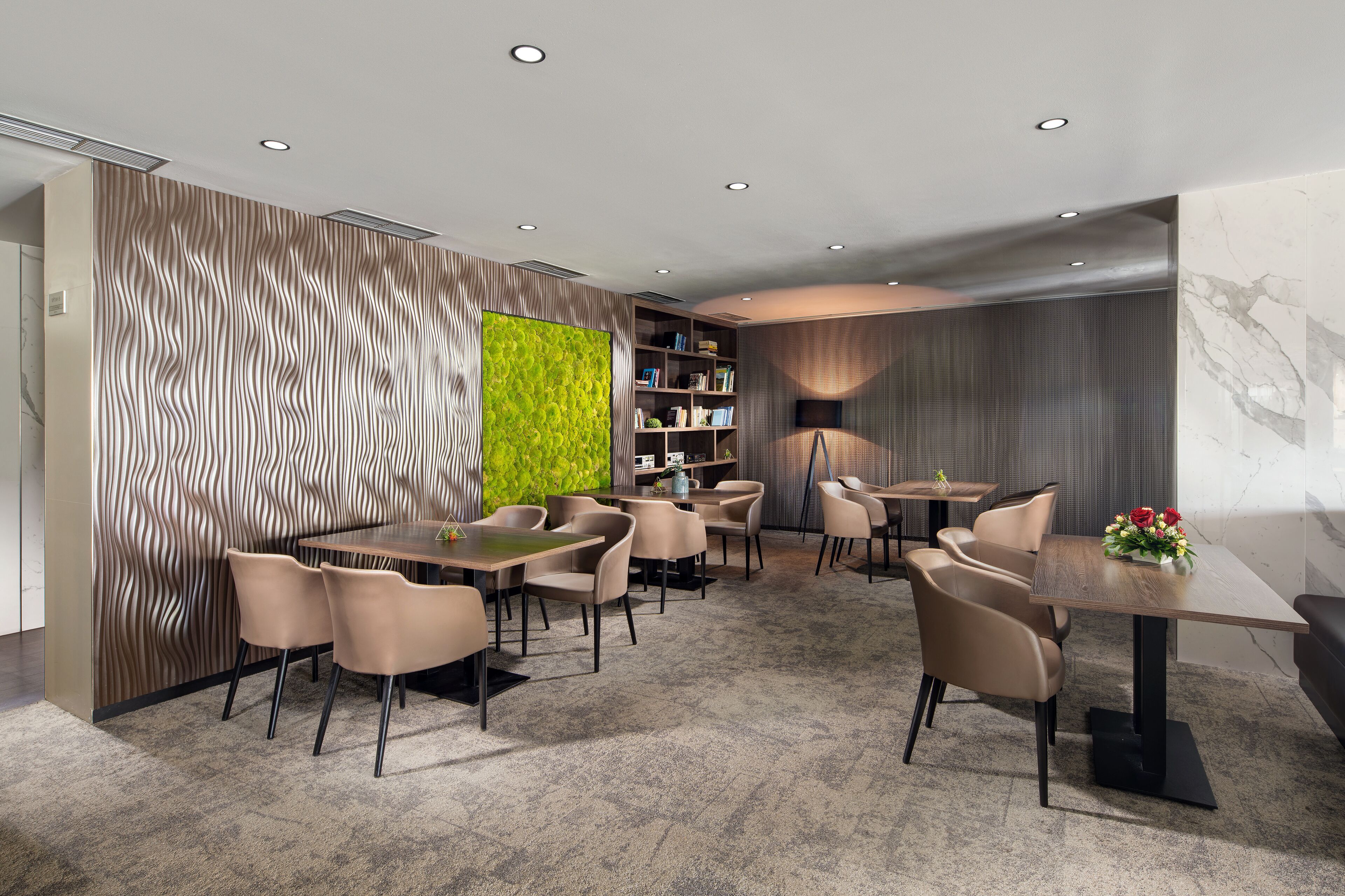 A modern dining area with a central table, surrounded by chairs, and a bookshelf with books.