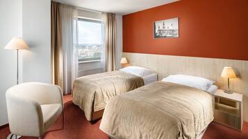 Et hotelværelse med to senge, en stol, et natbord, en lampe og et vindue med gardiner.