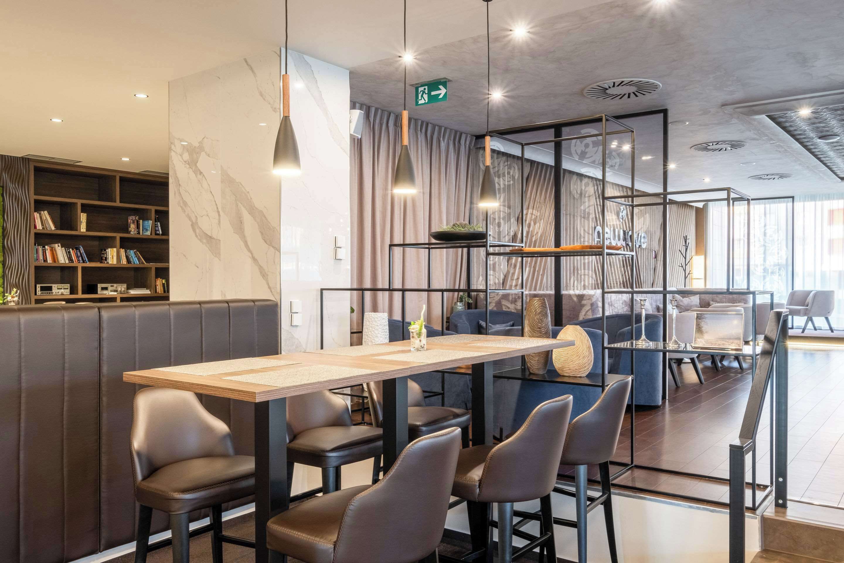 A modern restaurant with a long wooden table, leather chairs, and a bookshelf with books.
