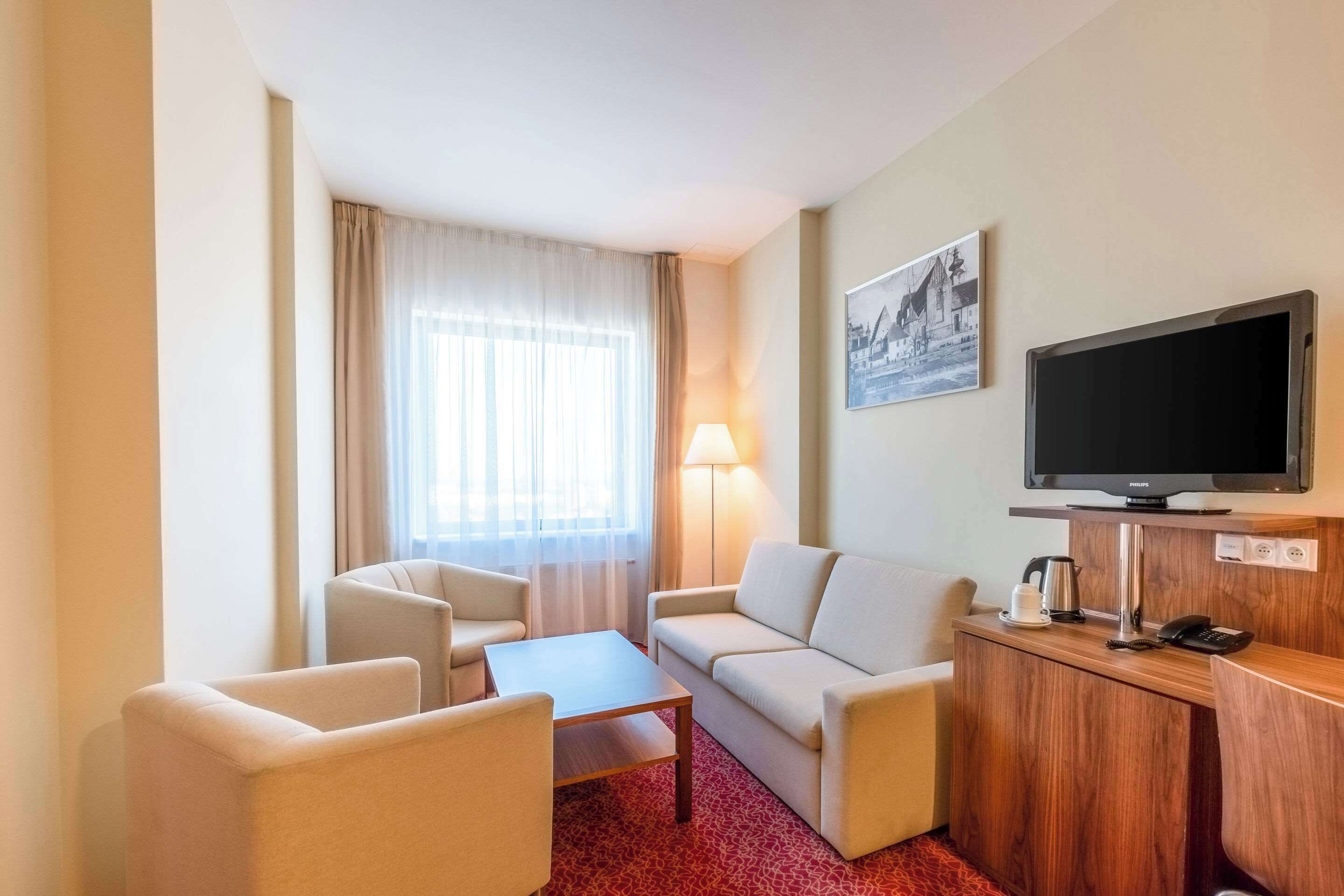 Habitación de hotel con sofá, dos sillones, una mesa de centro, televisor y lámpara.