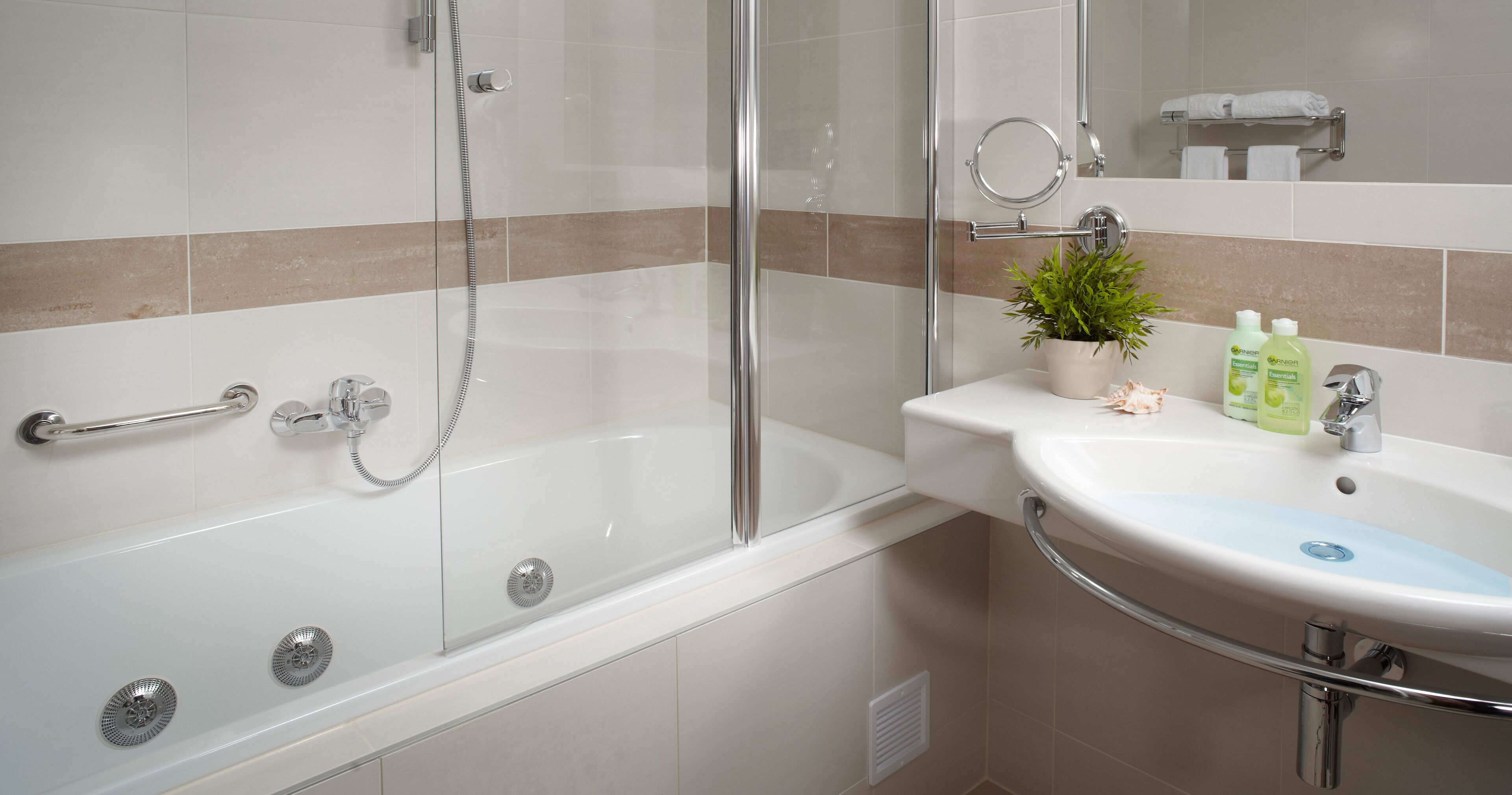 Un baño moderno con ducha de vidrio, un lavamanos blanco con detalles azules y una pequeña planta en maceta sobre el mueble.