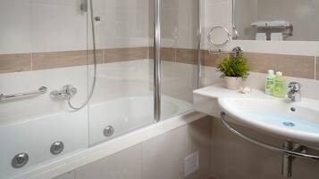 Un baño moderno con ducha de vidrio, un lavamanos blanco con detalles azules y una pequeña planta en maceta sobre el mueble.