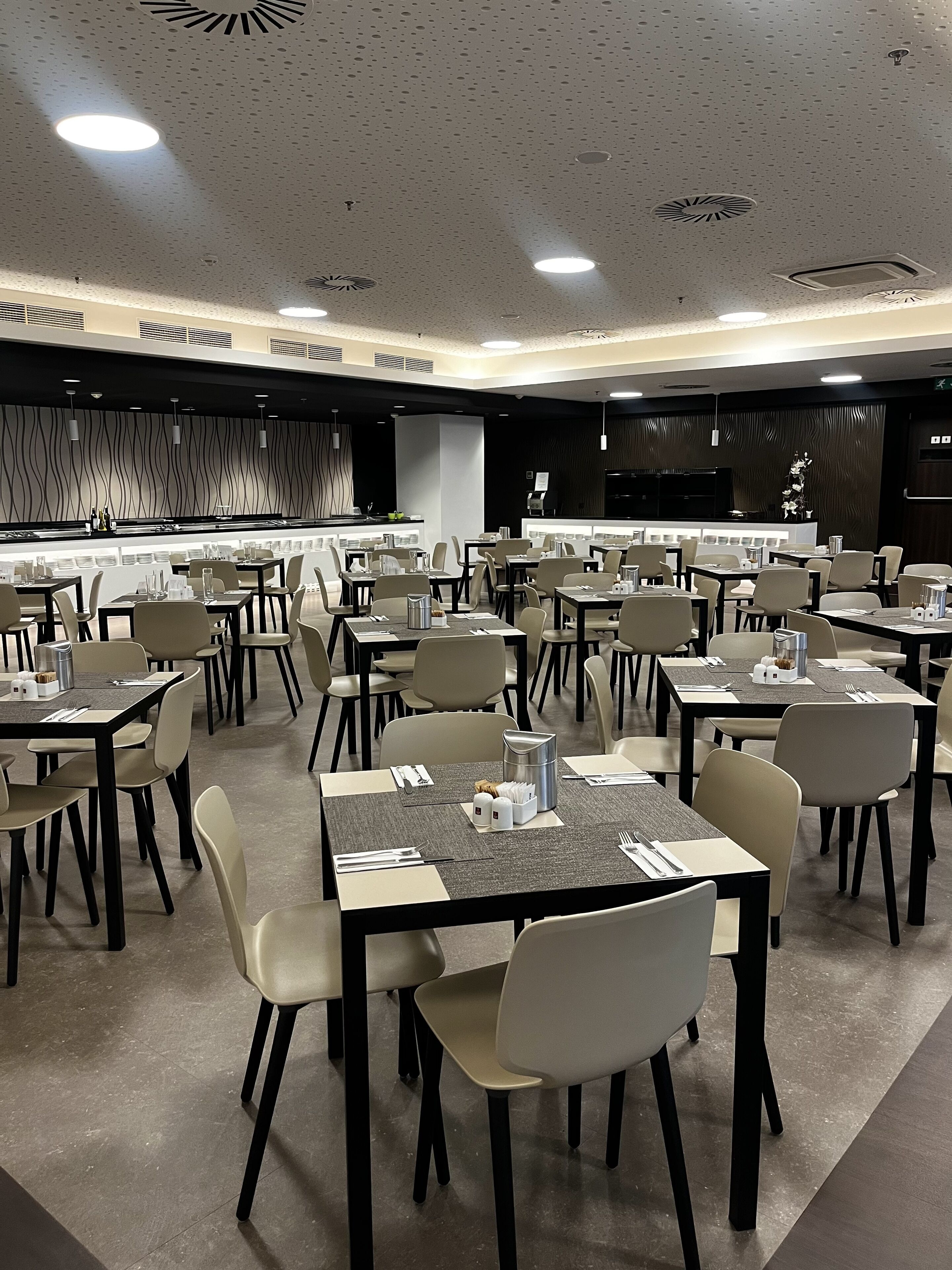 Un restaurante moderno con varias mesas y sillas, una barra con menú y una pared decorativa.