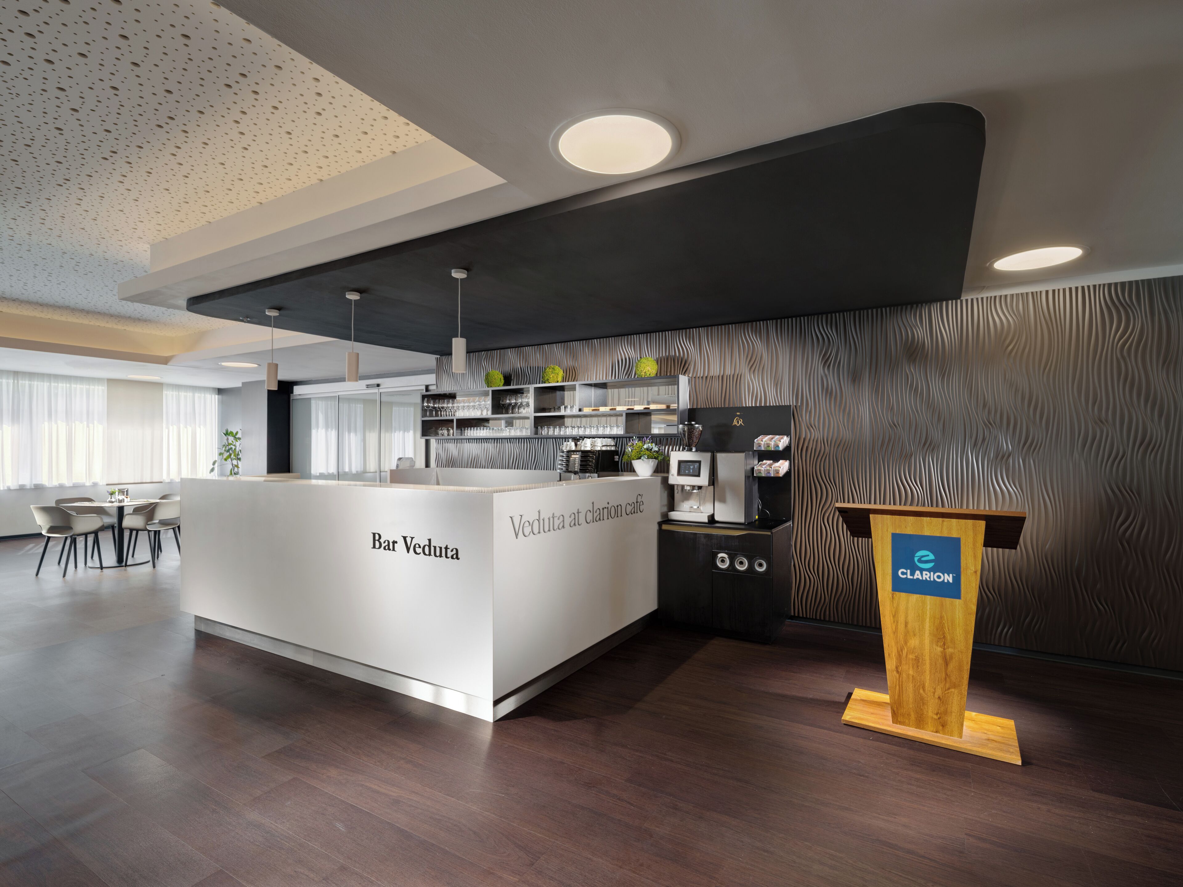 A modern bar area with a white counter, a coffee machine, and a wooden podium with the logo 'CLARION'.
