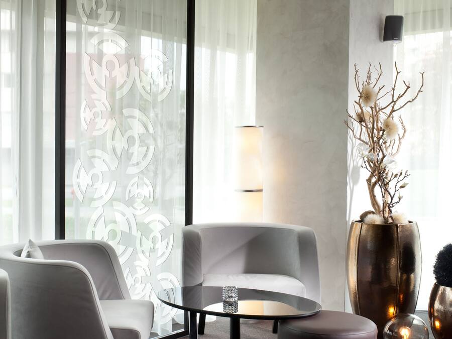 En moderne stue med et rundt glasbord, to grå sofaer, en stor vase med grene og en gulvlampe.