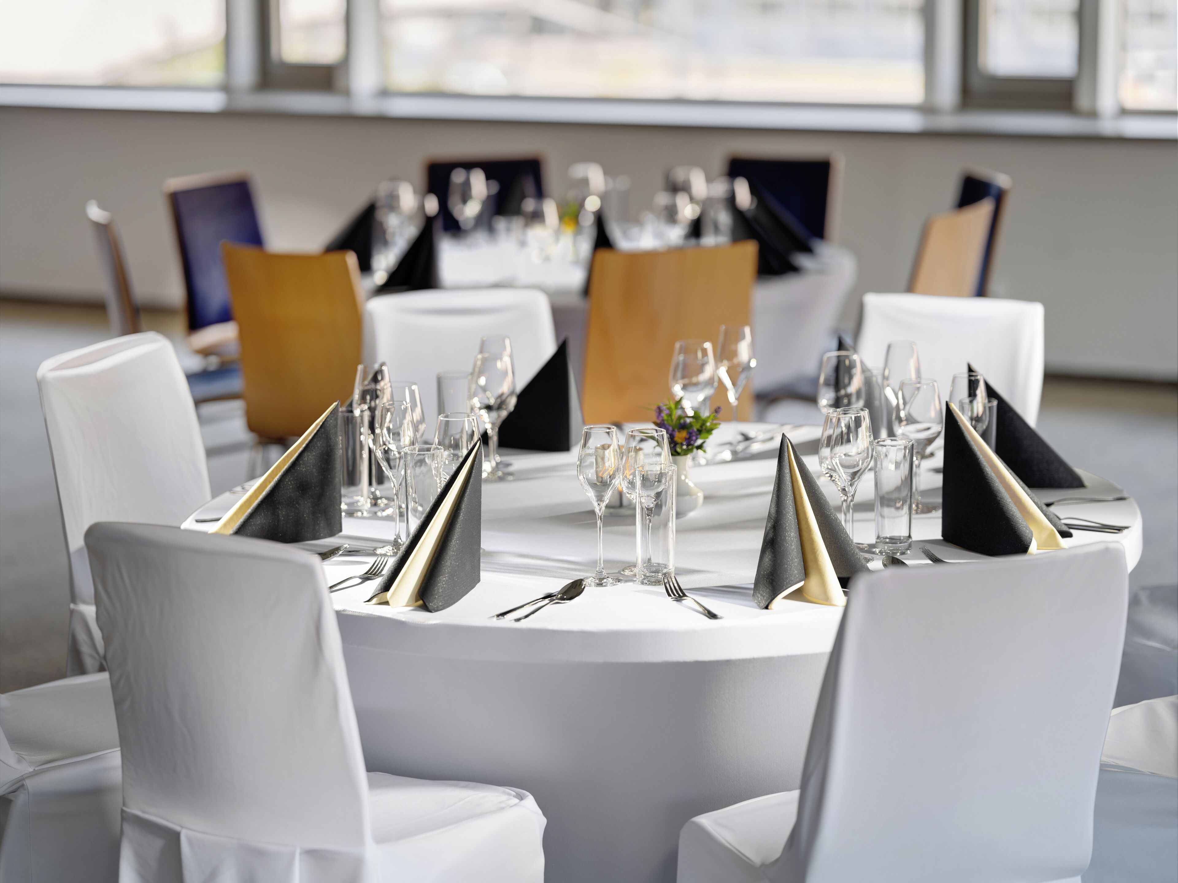 A formal dining setup with white tablecloths, silverware, and black napkins.