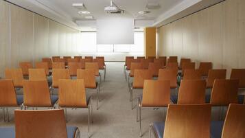 A conference room with rows of wooden chairs, a projector screen, and a large window.