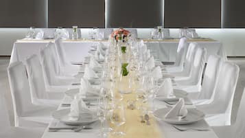Una larga mesa de banquete dispuesta con manteles blancos, sillas y cristalería, con un centro de mesa floral.