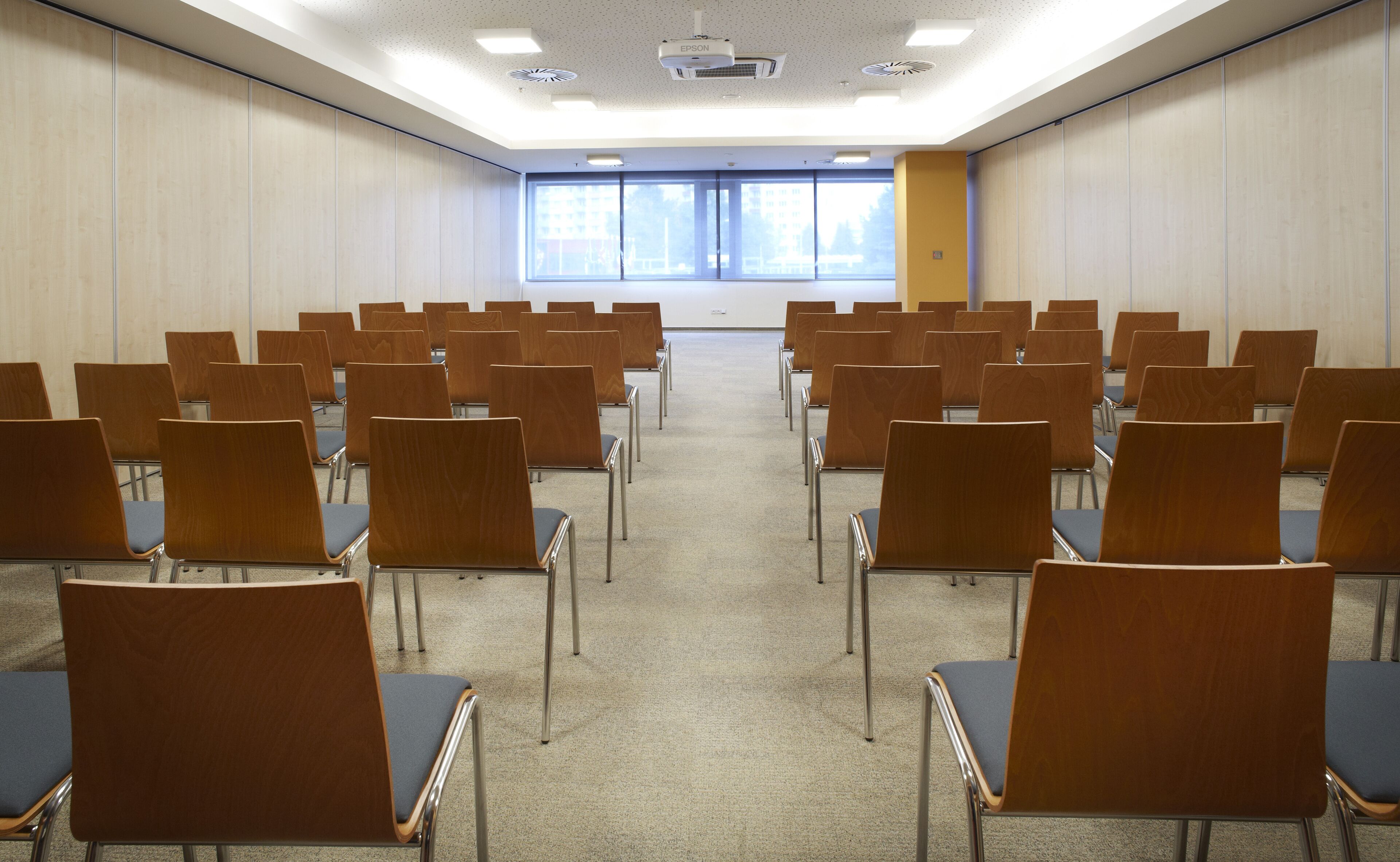 Une salle de conférence avec des rangées de chaises, un projecteur et de grandes fenêtres.