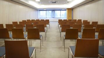 Une salle de conférence avec des rangées de chaises, un projecteur et de grandes fenêtres.