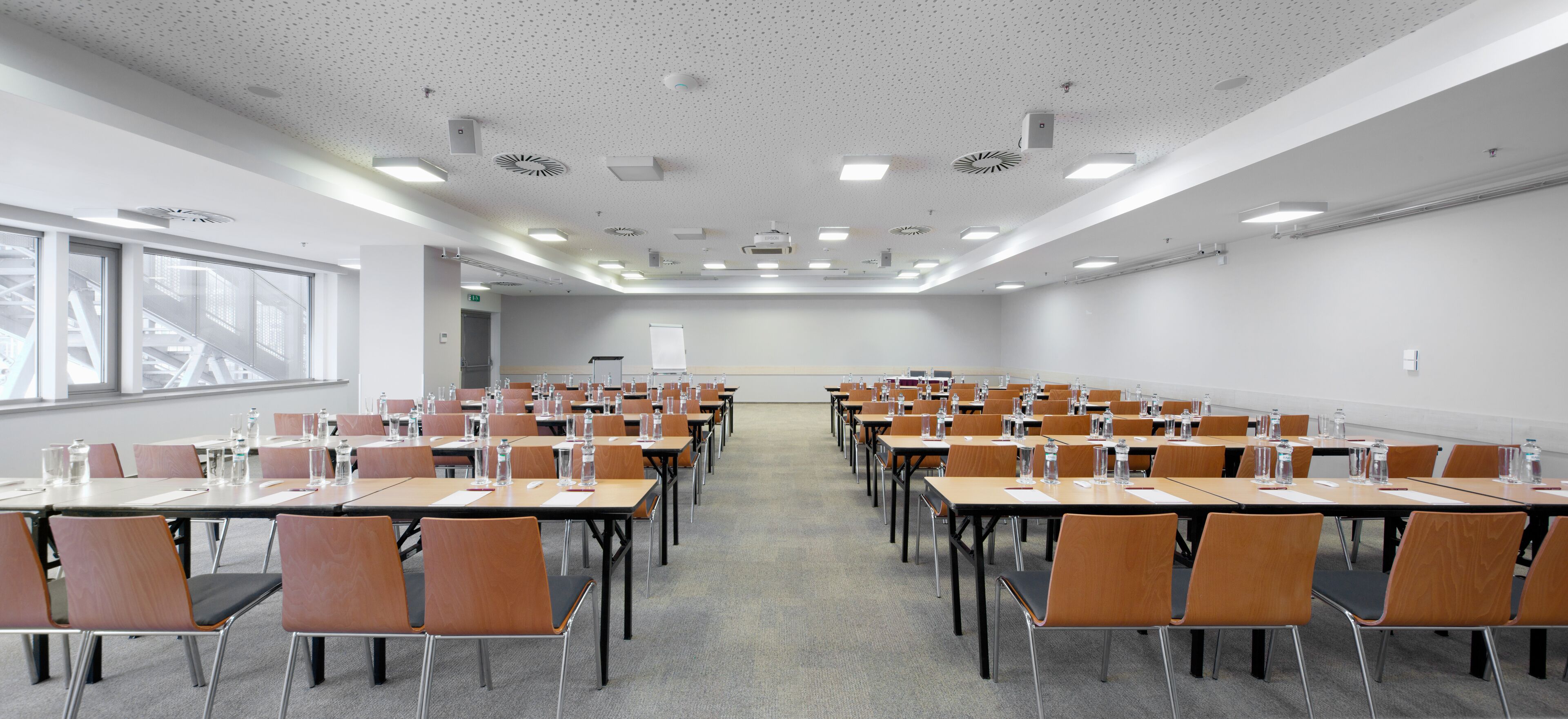 A conference room with rows of tables and chairs, equipped with water bottles and papers.