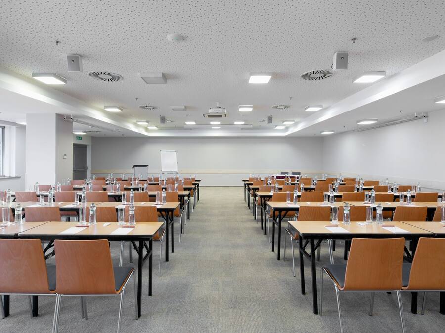 A conference room with rows of tables and chairs, equipped with water bottles and papers.