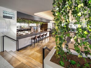 A modern bar area with a marble countertop, bar stools, and a green plant installation.