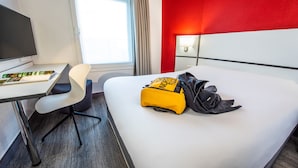 Une chambre d’hôtel avec un lit, un bureau et une chaise, un sac à dos North Face et une lampe.