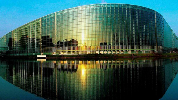 Un edifici modern de vidre amb façana corba que es reflecteix en una calma extensió d'aigua.