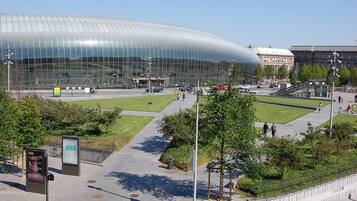 A modern glass building with a curved roof, surrounded by a landscaped area with pathways and benches.