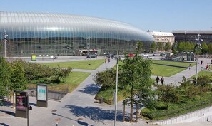 Un bâtiment moderne en verre, doté d’un toit incurvé, entouré d’un espace paysager agrémenté de sentiers et de bancs.