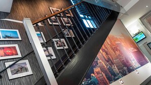 Un interior modern amb una escala, fotografies emmarcades a les parets i un mural gran amb una vista de la ciutat.