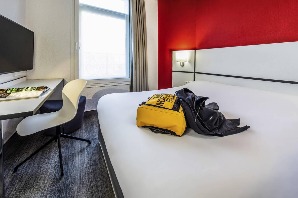 Une chambre d’hôtel avec un lit, un bureau, une chaise, une télévision et une fenêtre avec des rideaux.