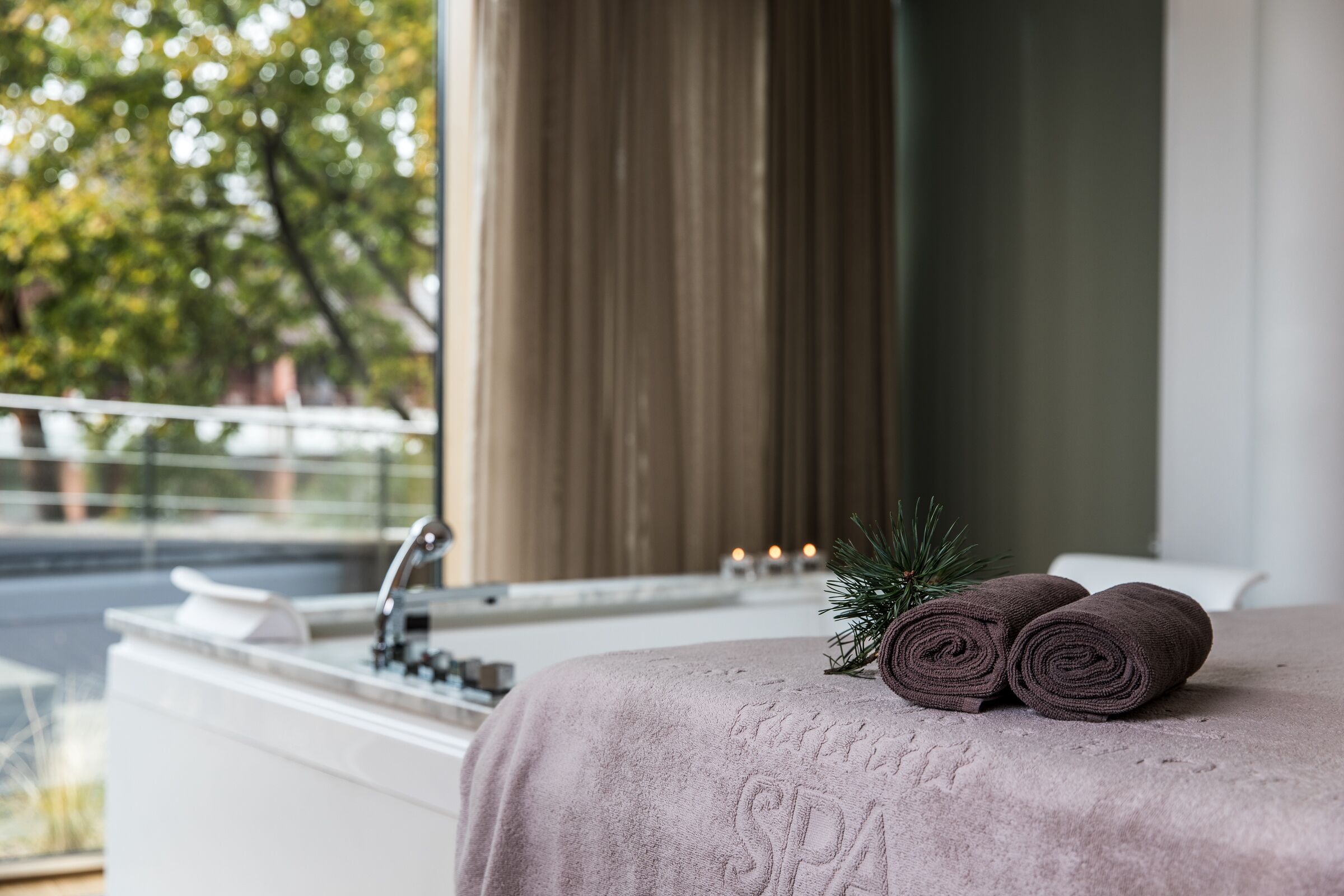Habitación de spa con bañera, toalla y una rama de pino.