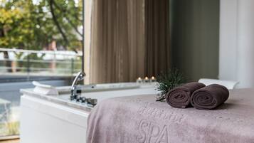 Habitación de spa con bañera, toalla y una rama de pino.