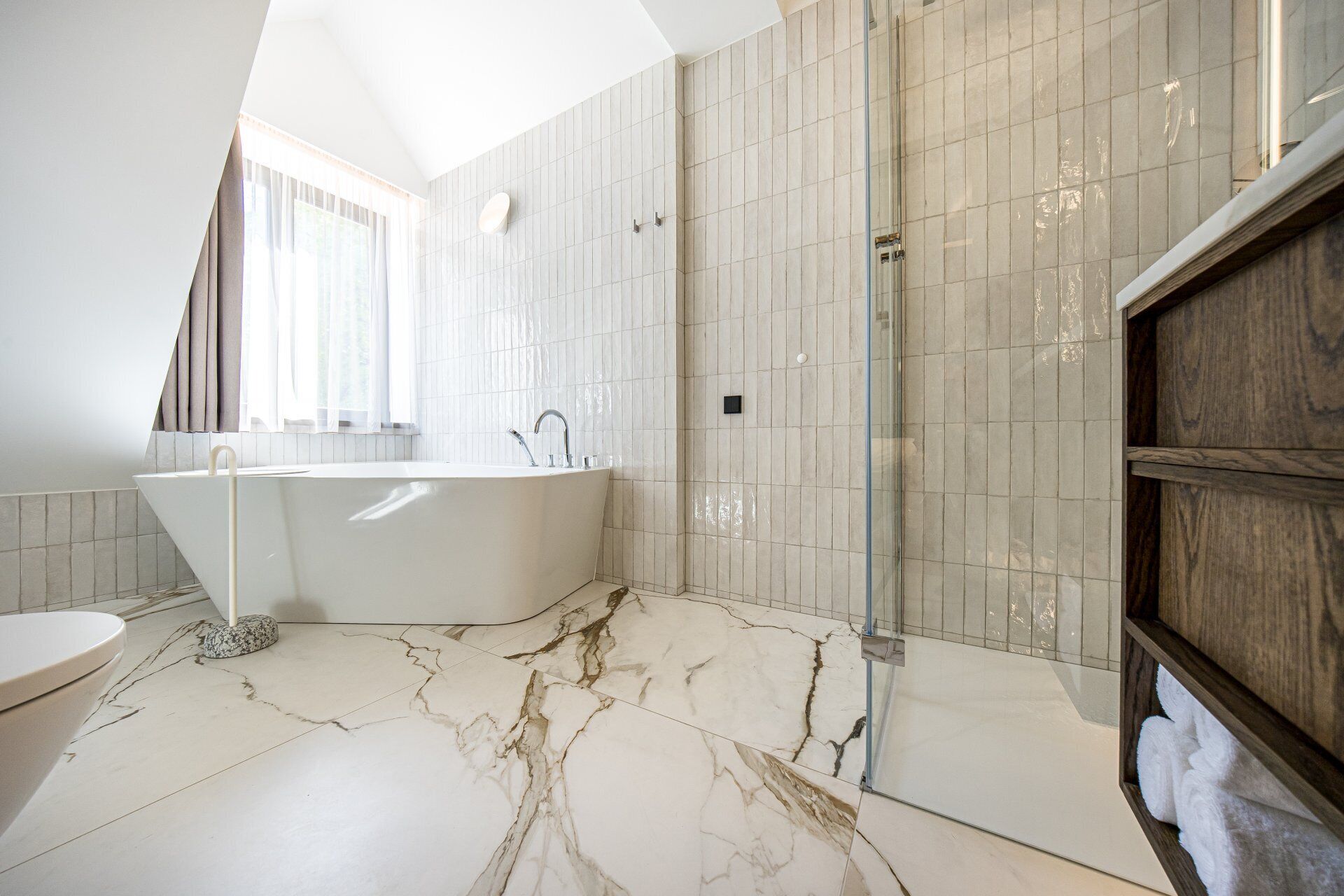 A modern bathroom with a freestanding bathtub, a glass shower enclosure, and a marble floor.
