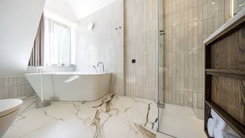 A modern bathroom with a freestanding bathtub, a glass shower enclosure, and a marble floor.