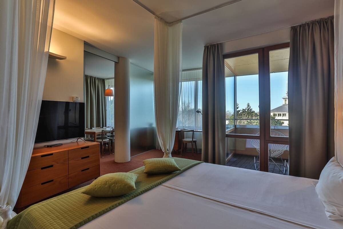 Ein Hotelzimmer mit Bett, Fernseher, Schreibtisch und einem Balkon mit Tisch und Stühlen.