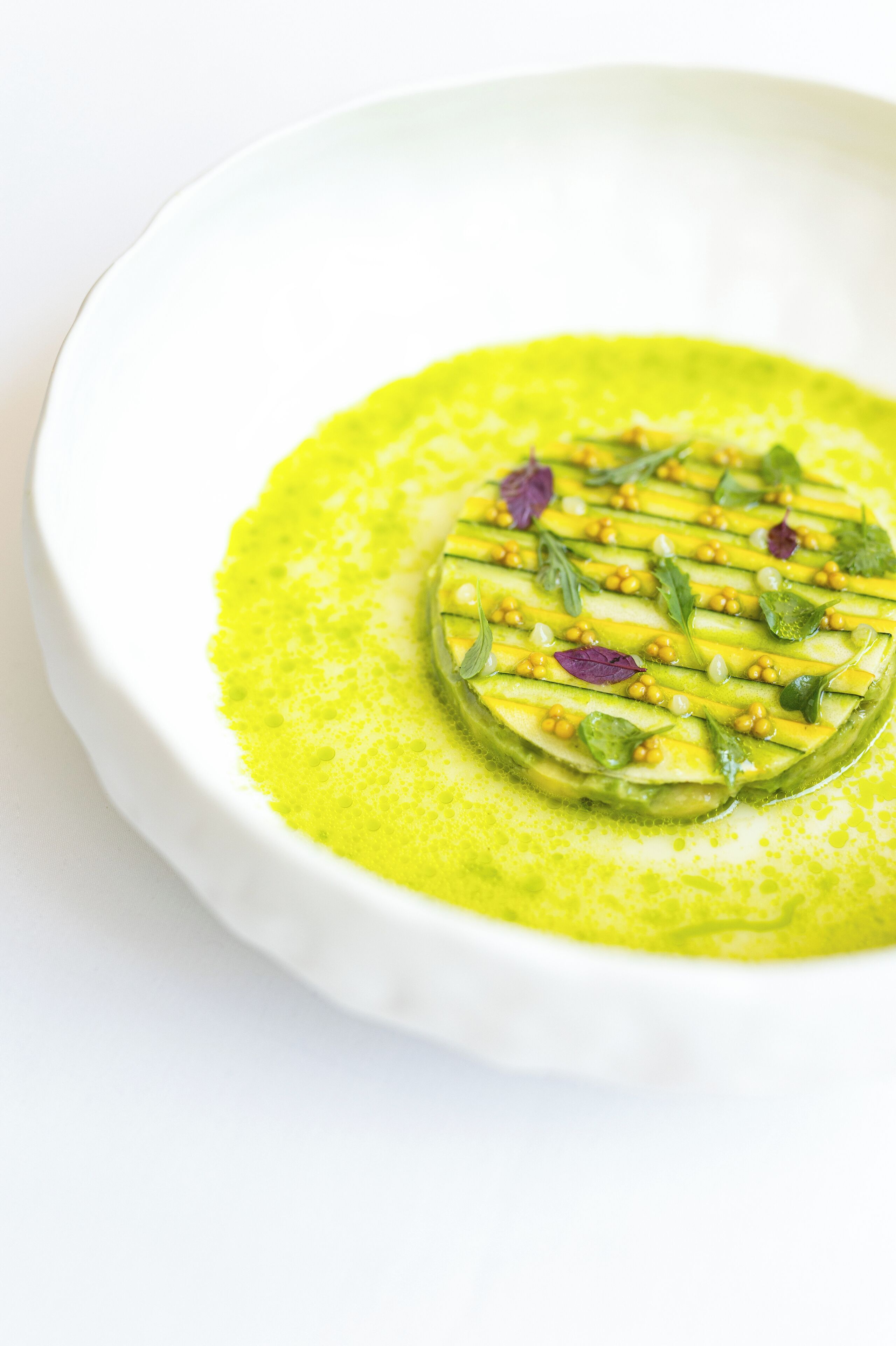 A white plate with a green dish, garnished with herbs and edible flowers.