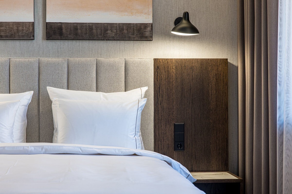 Ein modernes Hotelzimmer mit einem großen Bett, einem Kopfteil aus Holzpaneelen, einer Wandleuchte und einer Bedienkonsole.