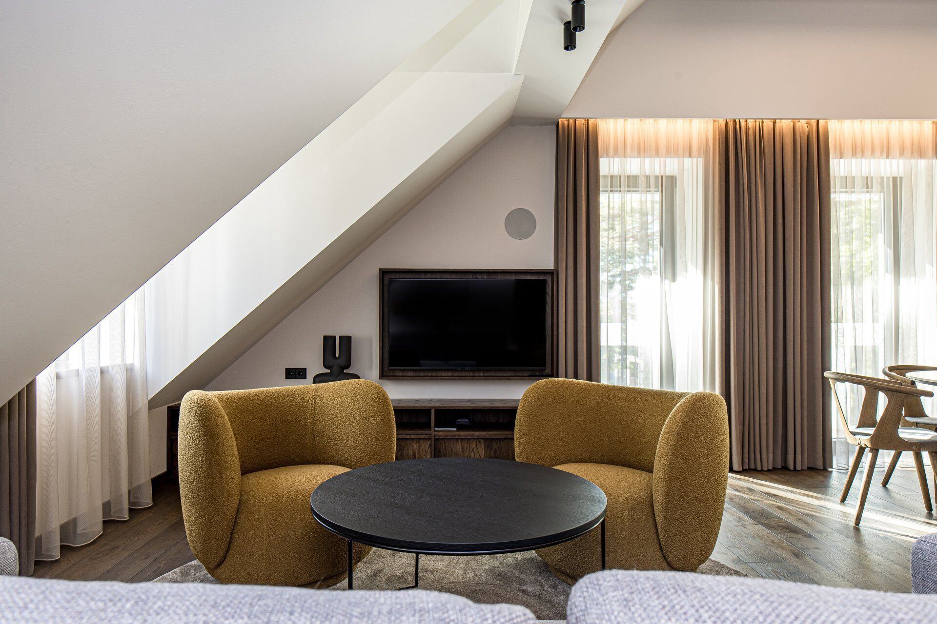 A modern living room with a TV, two armchairs, a round coffee table, and a dining area with wooden chairs.