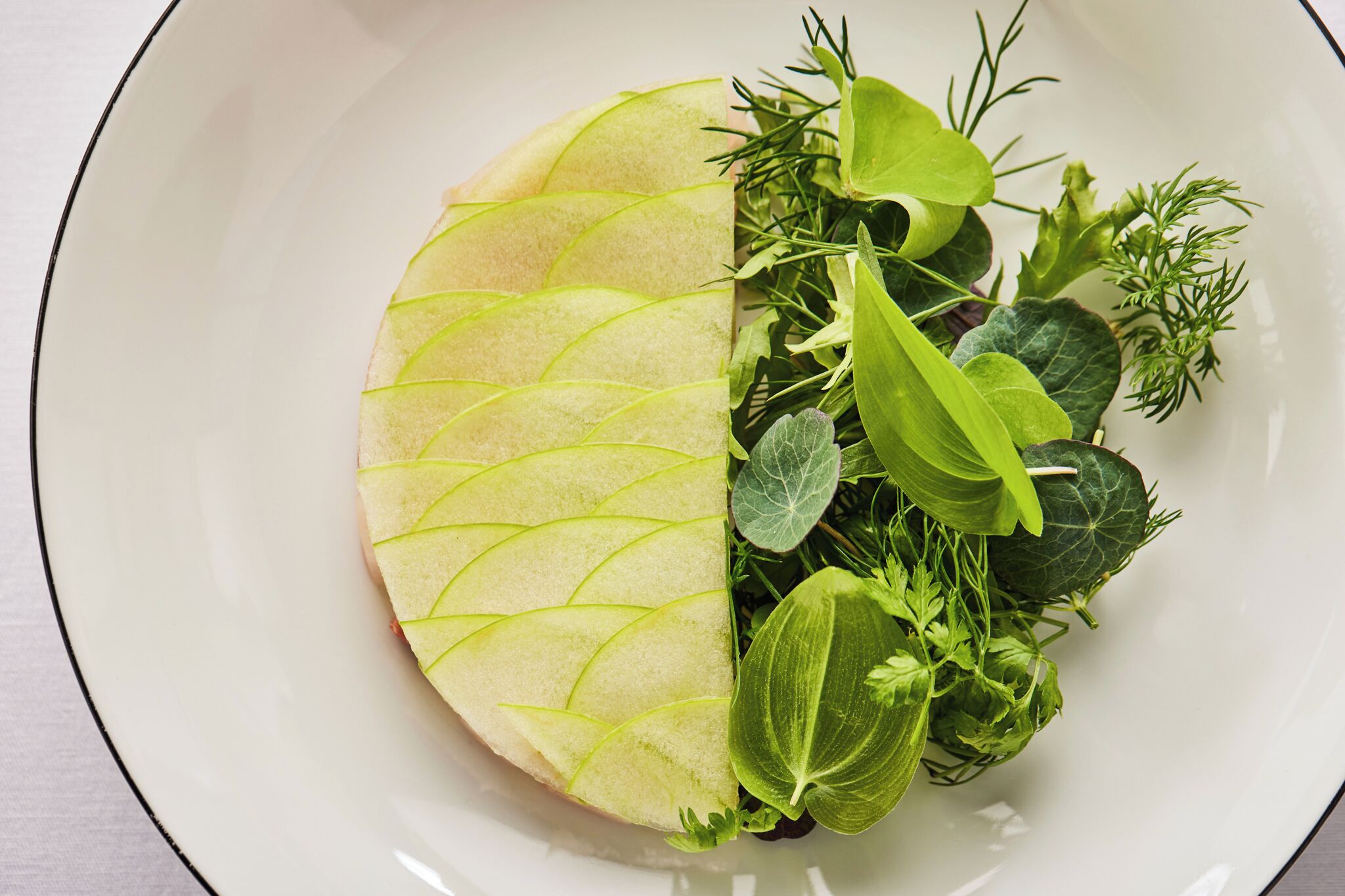 A white plate with a half-cut apple and various green herbs.