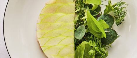 A white plate with a half-cut apple and various green herbs.