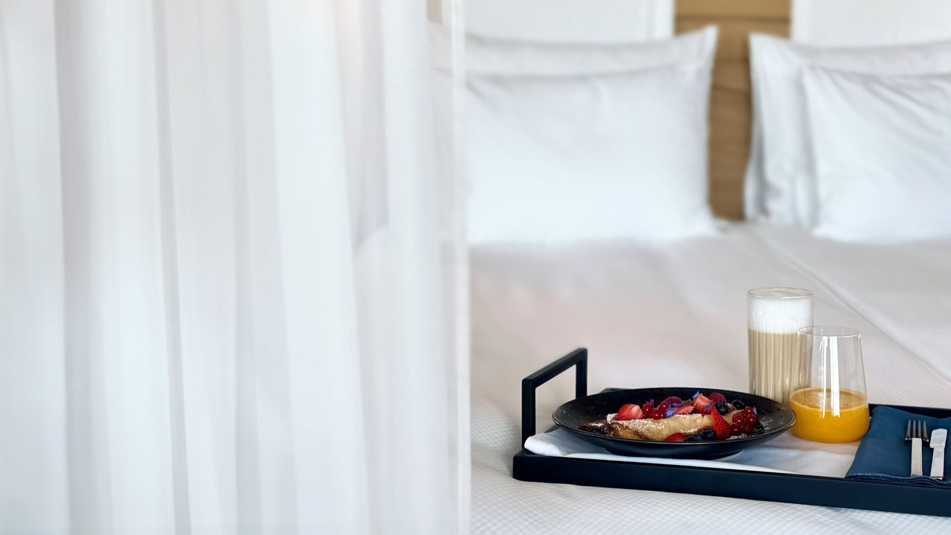 Un vassoio per la colazione ben apparecchiato con pancake, frutti di bosco e succo d'arancia su un letto d'hotel.