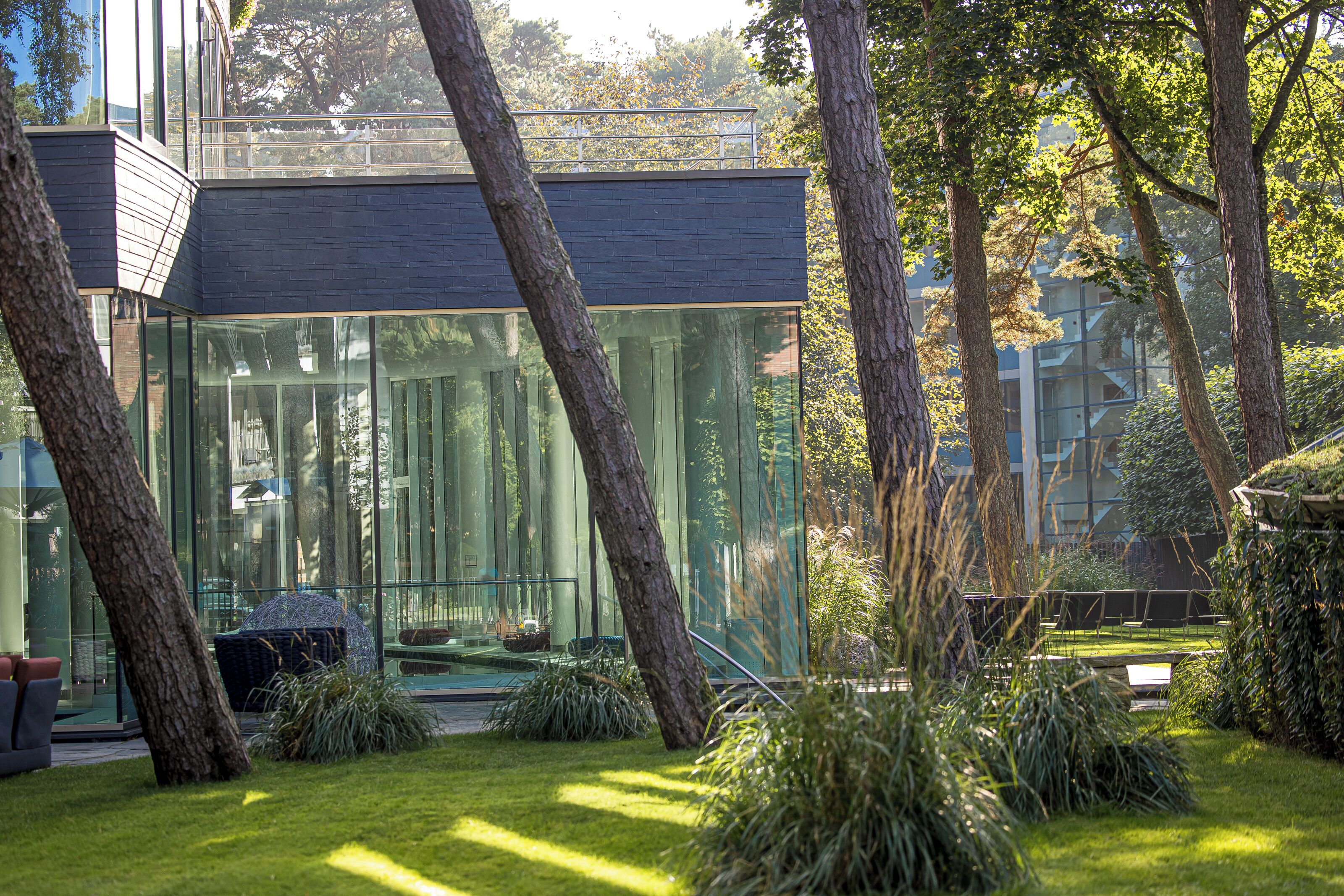Un bâtiment moderne doté de grandes fenêtres en verre, entouré d’arbres et d’une pelouse bien entretenue.
