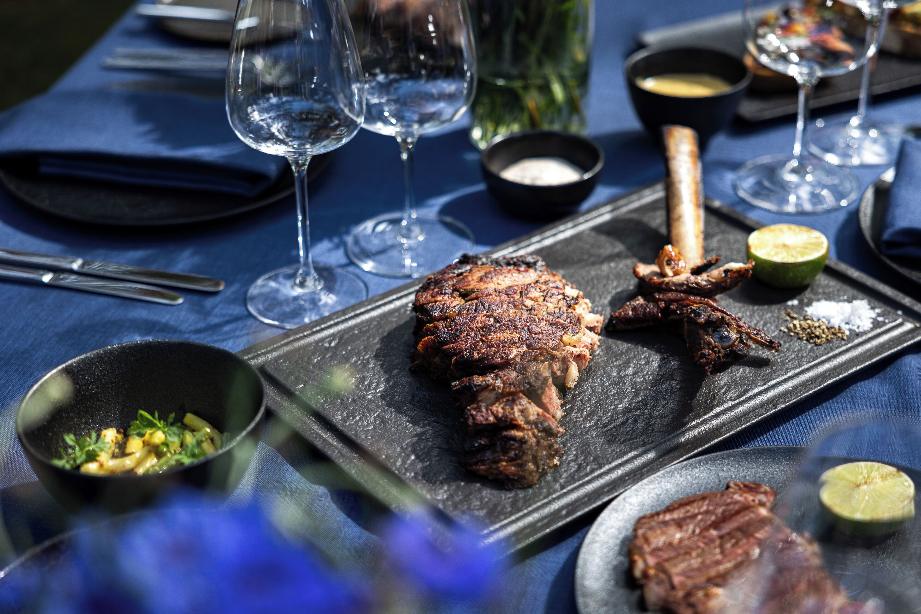 A dining table with a steak, a bowl of salad, and a glass of wine.