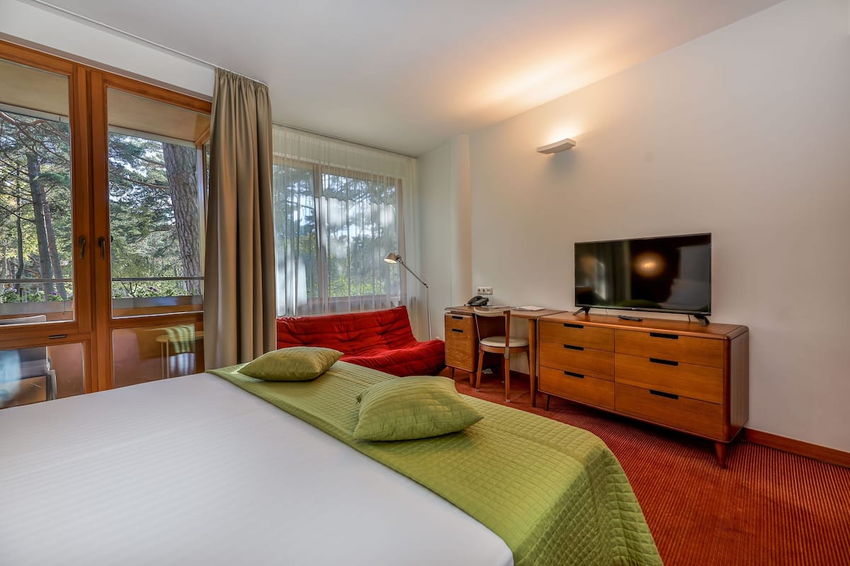 Ein Hotelzimmer mit einem großen Bett, einem Schreibtisch mit Stuhl, einem Fernseher und einem Fenster mit Vorhängen.