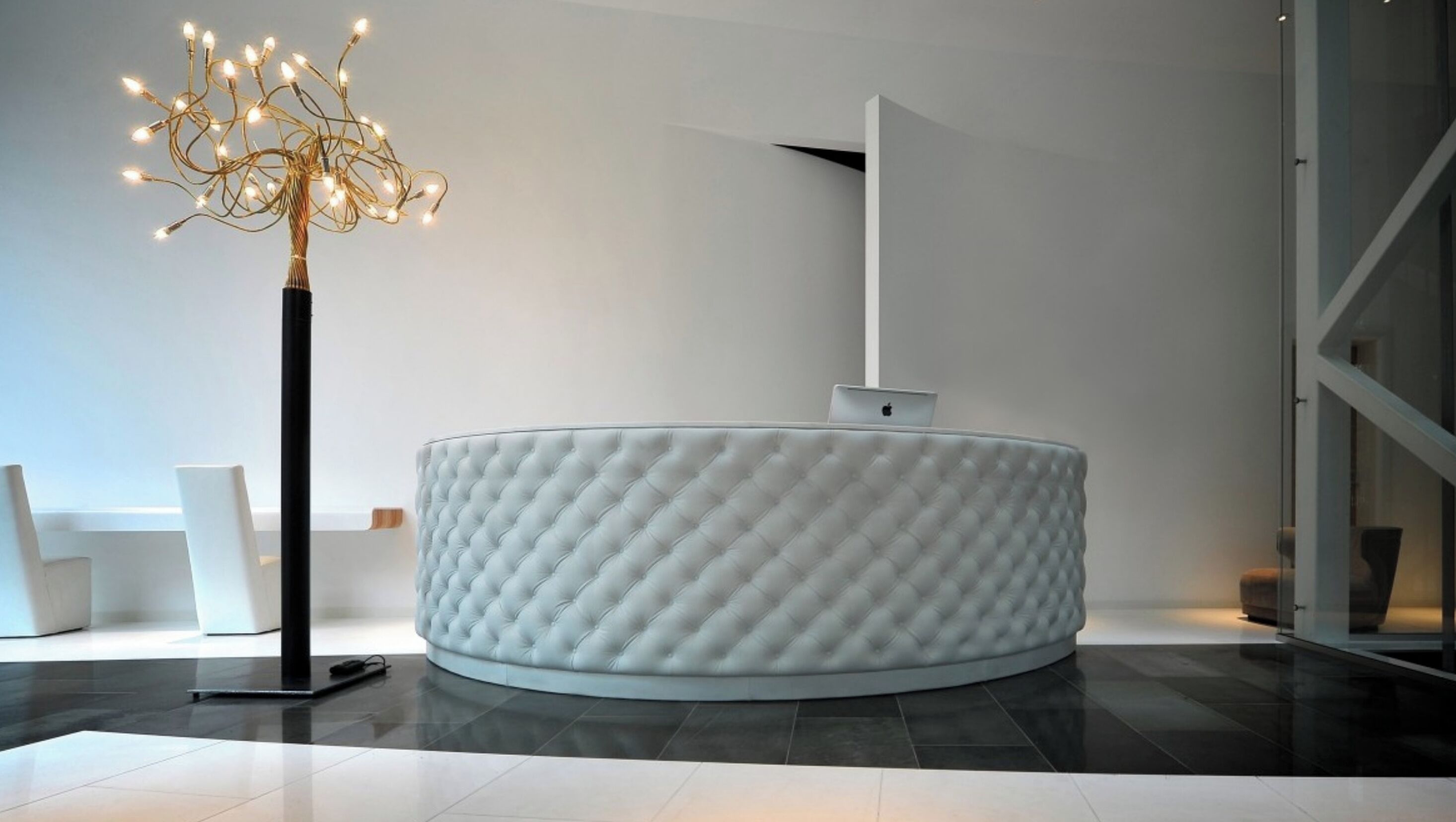 Ein moderner Empfangstresen mit Strukturverkleidung, eine freistehende Stehlampe und ein minimalistischer Einrichtungsstil.