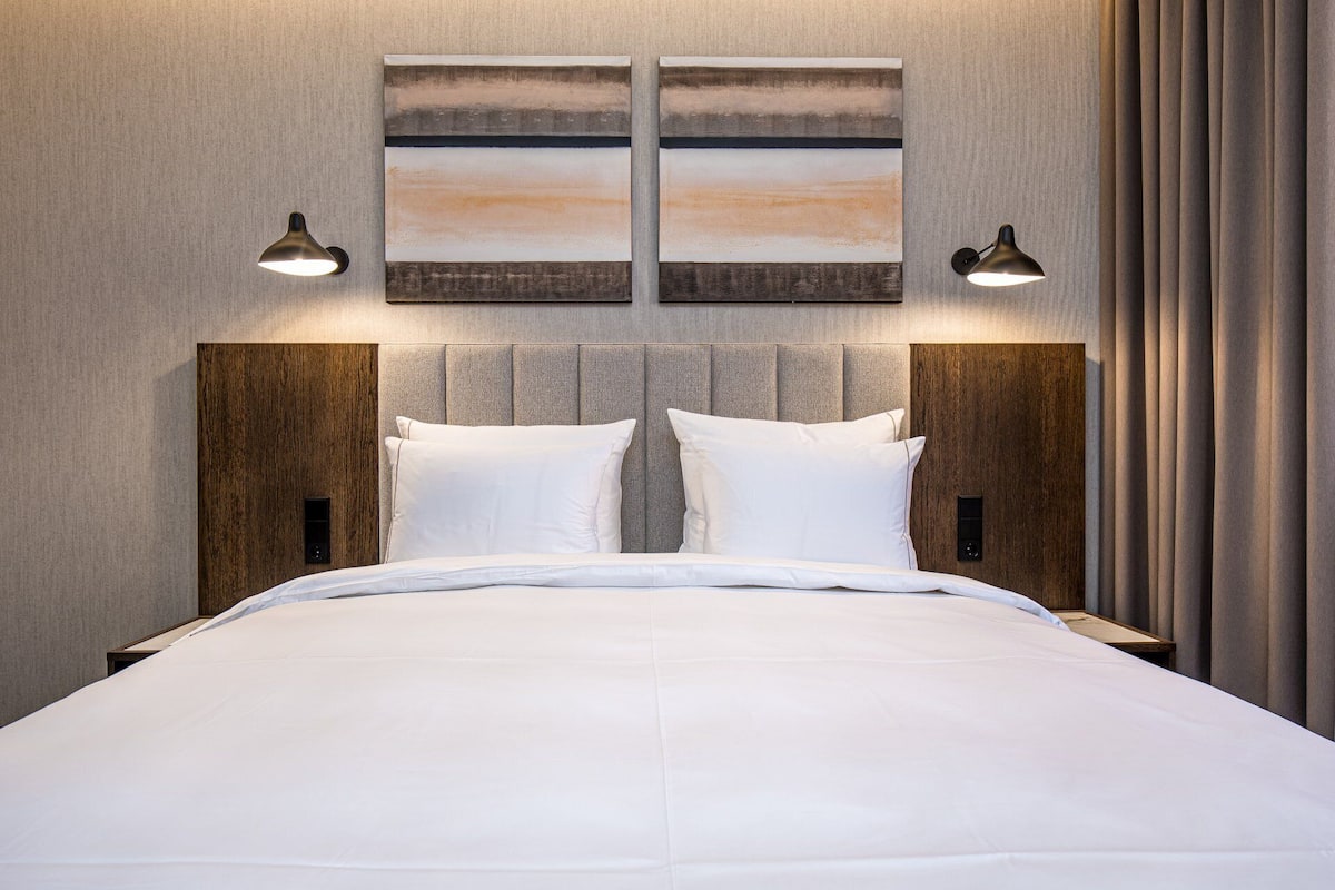 Ein Hotelzimmer mit einem großen Bett, zwei Nachttischen, einem Kopfteil und zwei Wandlampen.