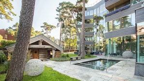 Een modern gebouw met een stenen zwembad, een houten hutje en grote bomen.