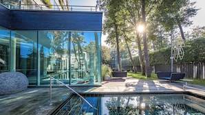 Een modern huis met een glazen gevel, een zwembad en een houten terras.