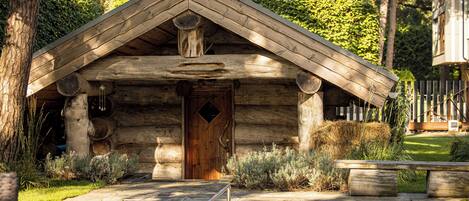 A rustic log cabin with a wooden door, a stone pathway leading to a small pool, and a wooden bench.